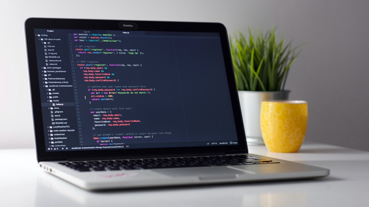 : Laptop prikazuje JavaScript programski kod sa Node.js i Express.js, pored žute šolje za kafu i biljke